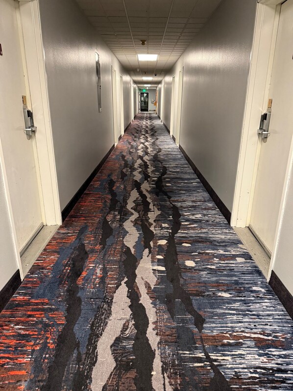 A hotel hallway with a patterned carpet, white walls, and doors on both sides. - Northwood Inn Prairie Du Chien (Prairie Du Chien)