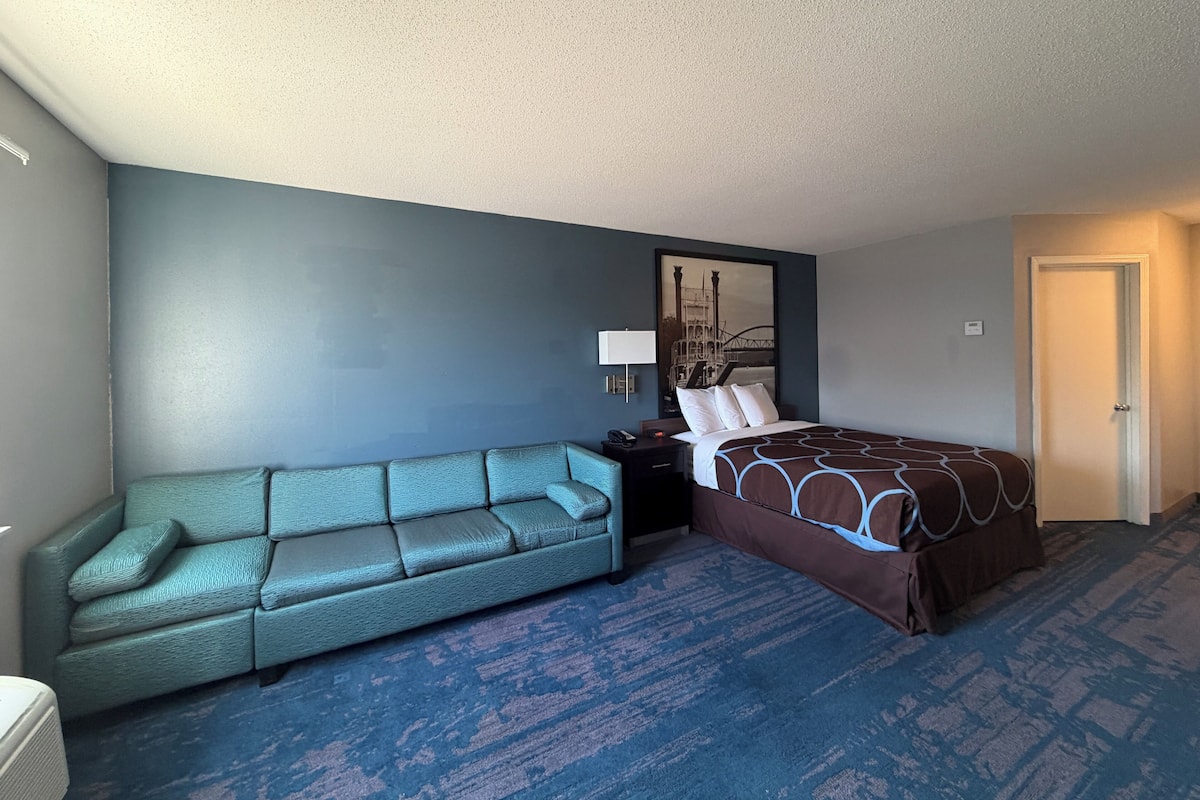 A hotel room with a bed, a sofa, a nightstand, and a wall-mounted lamp.
