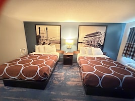 Habitación de hotel con dos camas, una mesita de noche, una lámpara y dos cuadros en la pared.