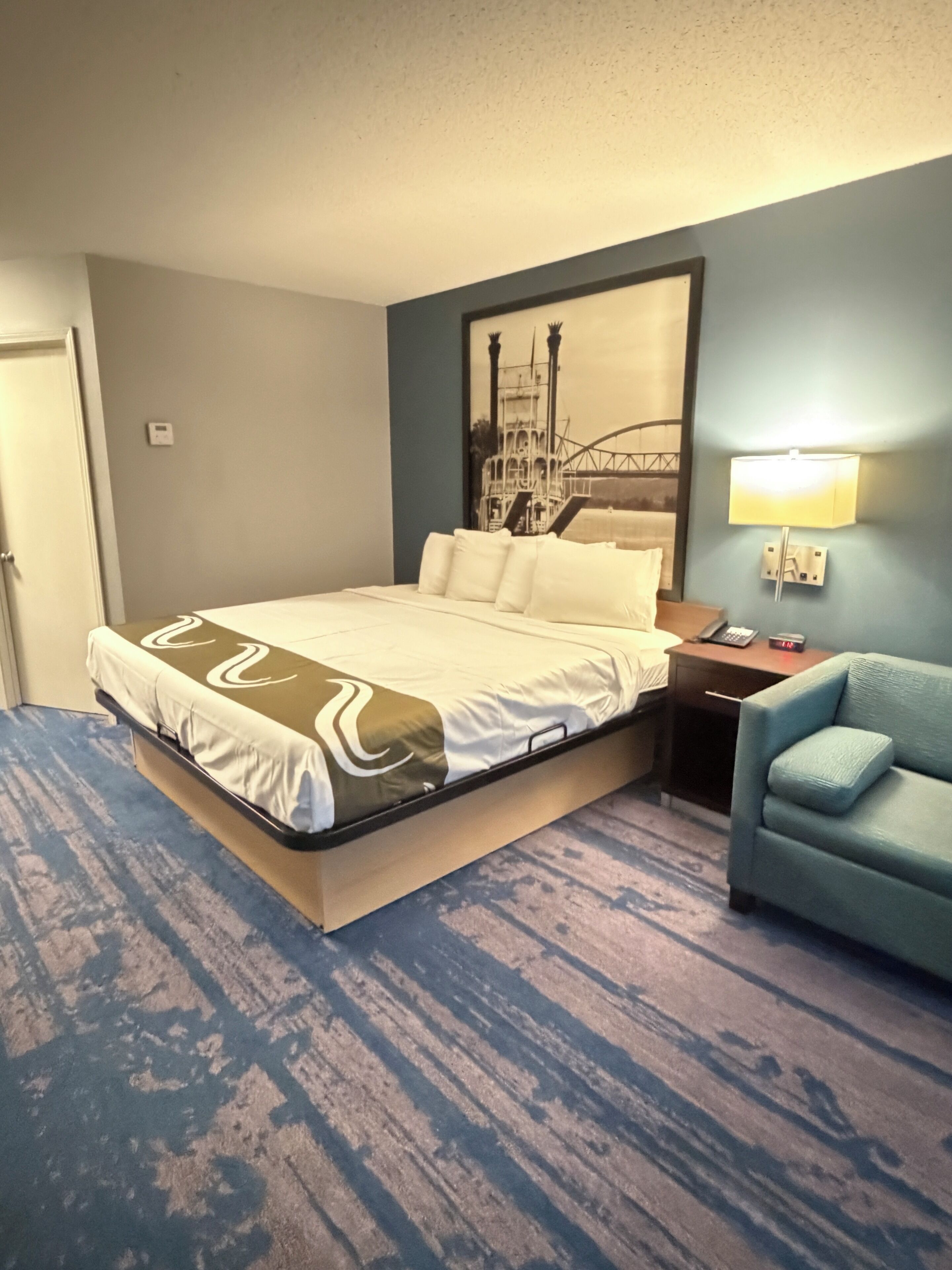 A hotel room with a bed, a nightstand, a lamp, and a chair.