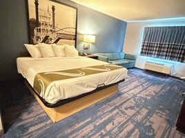 A hotel room with a large bed, a sofa, a lamp, and a window with curtains.