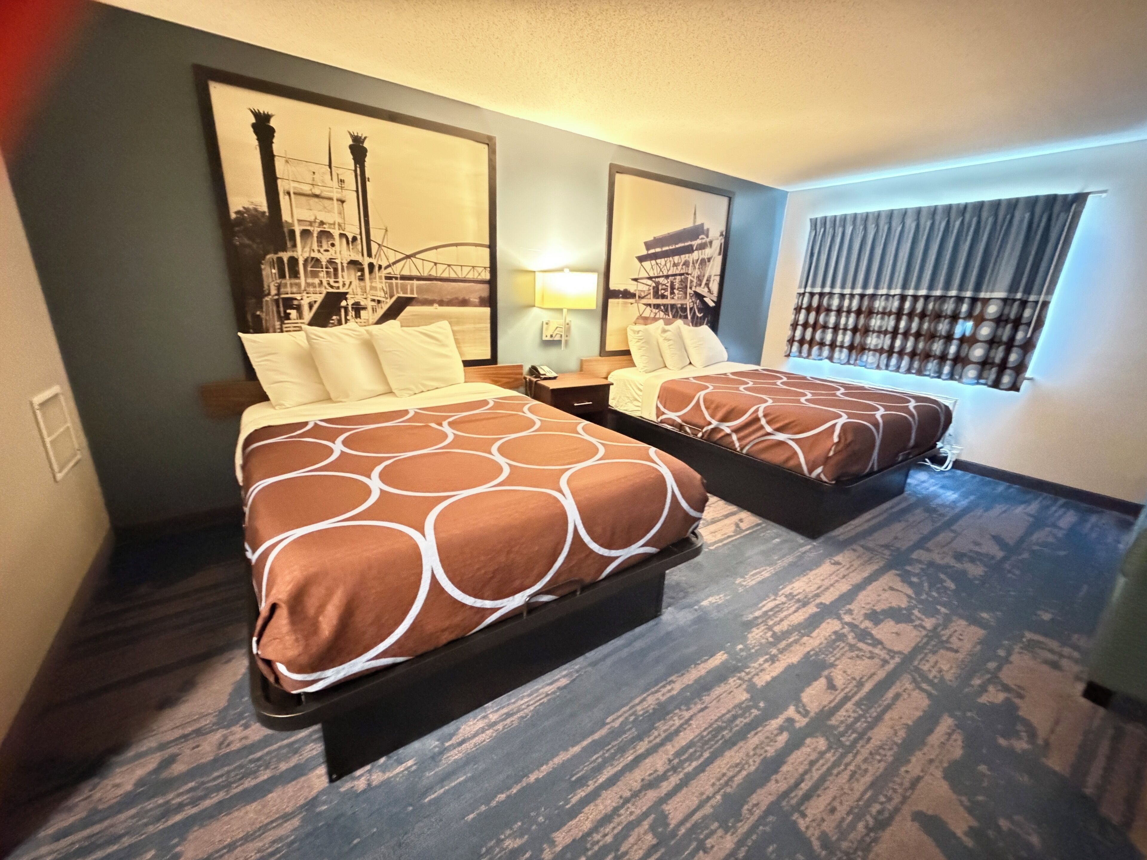 A hotel room with two beds, a large mirror, a nightstand, and a window with curtains.