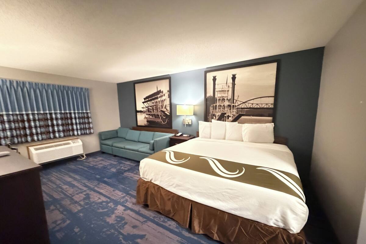 A hotel room with a large bed, a sofa, a desk, and a window with curtains.