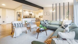 Ein modernes Wohnzimmer mit einer Couch, Sesseln und einem Couchtisch. Im Hintergrund ist eine Küchenzeile zu sehen.