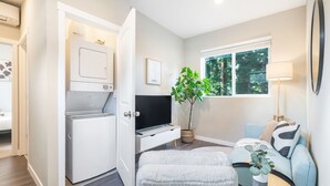 Un espacio habitable compacto con zona de lavandería, un sofá, una mesa de centro y una planta en maceta.