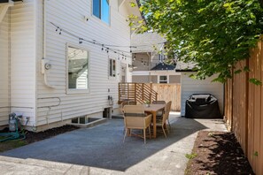 A patio with a table and chairs, a barbecue grill, and a wooden fence. - AC · Walks to Cap Hill · Parking · Newly Renovated (Seattle)
