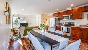 A modern kitchen with wooden cabinets, stainless steel appliances, and a dining area with a dark table and grey chairs.