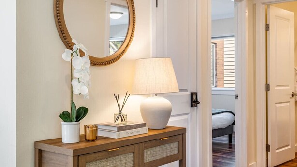 A hallway with a wooden console table, a white lamp, a mirror, and a potted orchid.