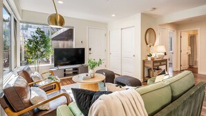 A modern living room with a large flat-screen TV, comfortable seating, a coffee table, and a view of the outdoors.