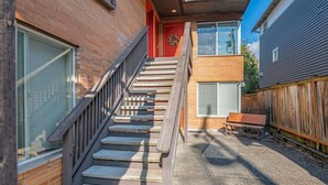 A residential building with a brick exterior, a wooden staircase, and a wooden bench in the yard.