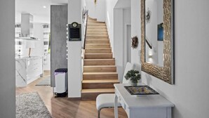 Een modern interieur met een houten trap naar een hoger niveau, een witte consolese tafel met een decoratief object, en een grote spiegel met een gestructureerde lijst.