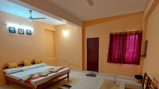 Un dormitorio con cama, ventilador de techo, mesa con sillas y ventana con cortinas.