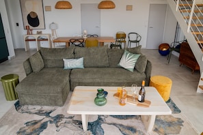 Ein modernes Wohnzimmer mit einer Eckcouch, einem Esstisch und einer Treppe.