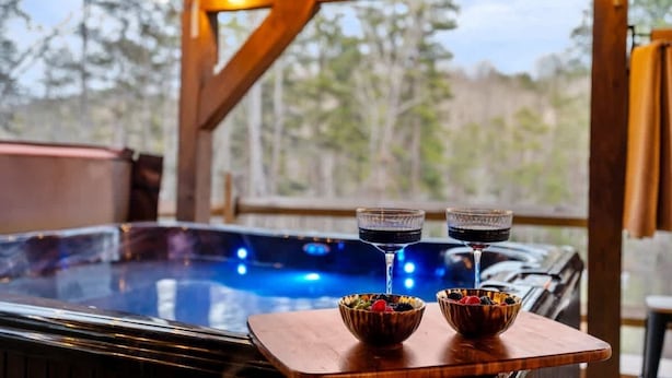 A hot tub with two bowls of fruit and two glasses of a dark beverage.