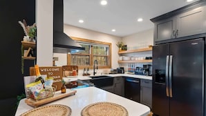 A modern kitchen with a large island, black refrigerator, and wooden shelves.