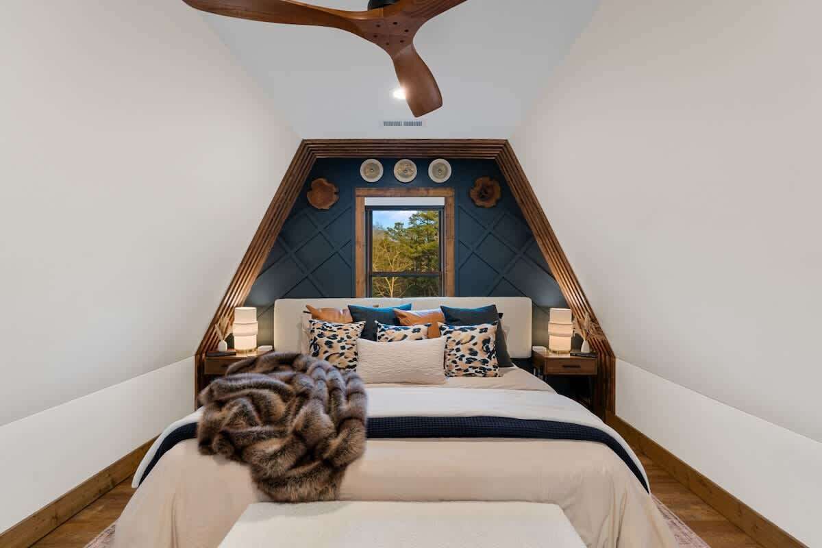 A bedroom with a sloped ceiling, a bed with a white and navy bedding, and a wooden headboard.