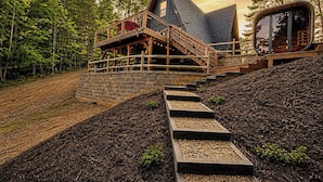 A modern house with a wooden deck, a stone retaining wall, and a circular glass structure.