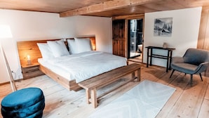 Een slaapkamer met een houten bed, een bankje, een stoel, een kleine tafel en een schilderij aan de muur.