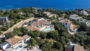 Vue aérienne d’un quartier résidentiel situé sur la côte, avec des maisons, une piscine et une vue sur la mer.