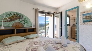 Une chambre à coucher avec un lit, des oreillers, une table de chevet avec une lampe, un élément décoratif mural et une vue sur l’extérieur.