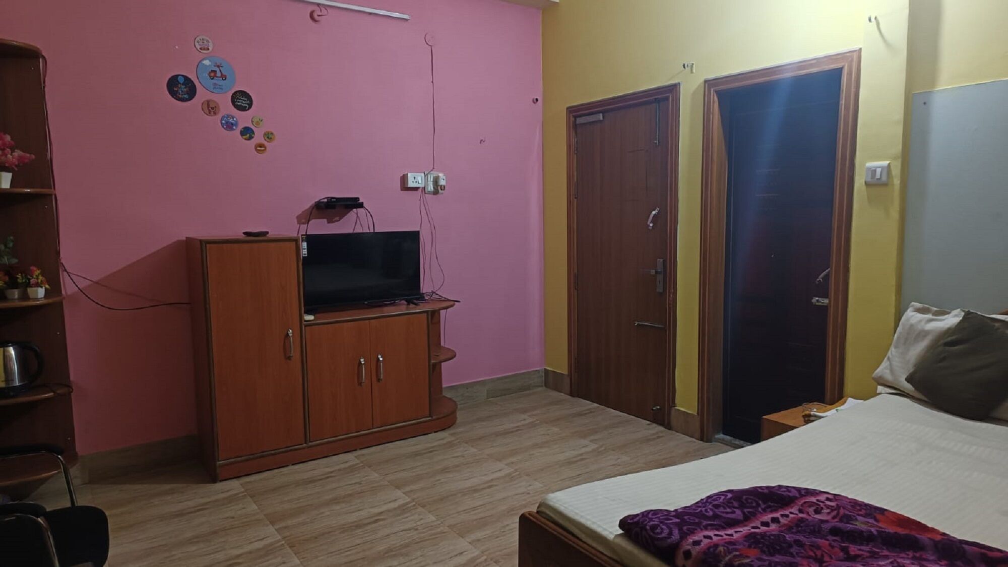 A bedroom with a bed, a TV on a wooden cabinet, a wardrobe, and a door.