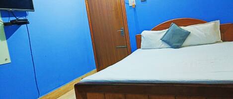 Un dormitorio con cama de madera, televisión en la pared y una puerta.