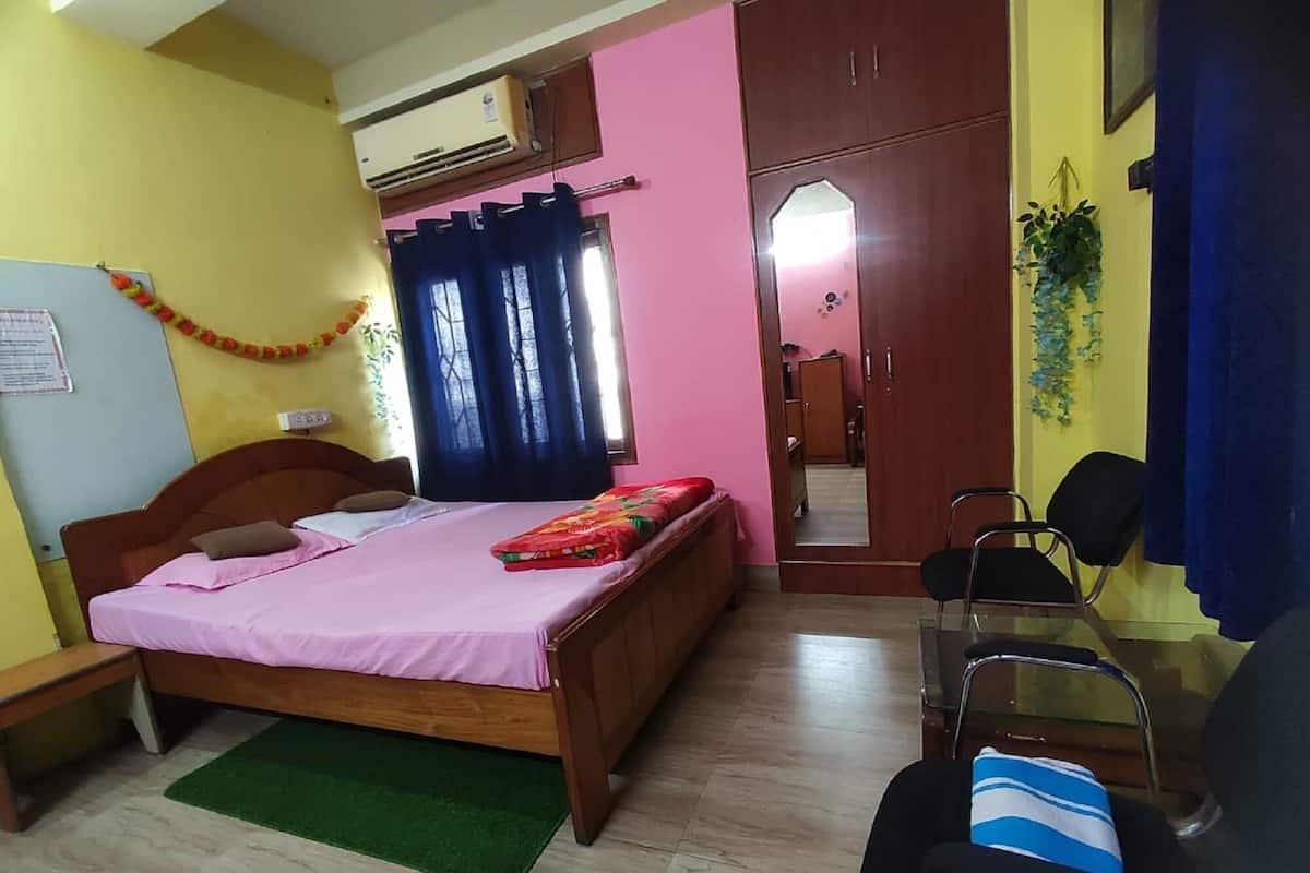A bedroom with a bed, a desk, a chair, an air conditioner, and a wardrobe.