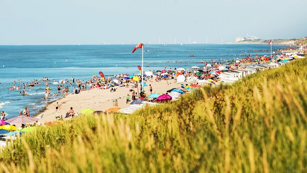 Une plage avec des gens, des parasols et des bateaux.