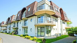 Un immeuble résidentiel moderne à plusieurs étages, doté de balcons, de grandes fenêtres et d’une pelouse bien entretenue.