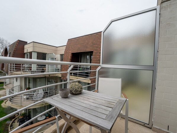 A balcony with a wooden table, white chairs, and a decorative vase. - Deauville II with parking by Interhome (Bredene)