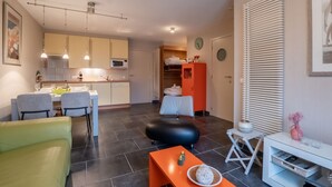 Un espace de vie compact comprenant un coin cuisine, un coin repas et un espace détente avec un canapé et une table.