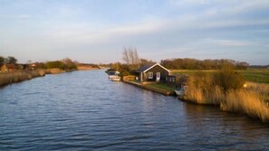 A riverside house with a dock, surrounded by fields and trees. - Host Stay Tide Time (Great Yarmouth)