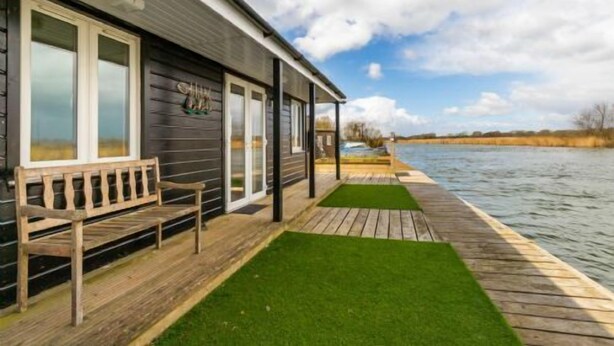 A wooden dock extending into a body of water, with a building featuring large windows and a bench on the dock. - Host Stay Tide Time (Great Yarmouth)