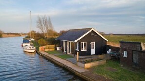 A small house by a canal with a boat docked nearby. - Host Stay Tide Time (Great Yarmouth)