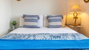 A bed with a blue and white striped blanket, two pillows with similar stripes, a small plant on a nightstand, and a wall-mounted lamp. - Host Stay Tide Time (Great Yarmouth)