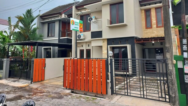 Un edificio residenziale di due piani con ingresso chiuso da cancello, un balcone e un cartello pubblicitario di un'attività locale.