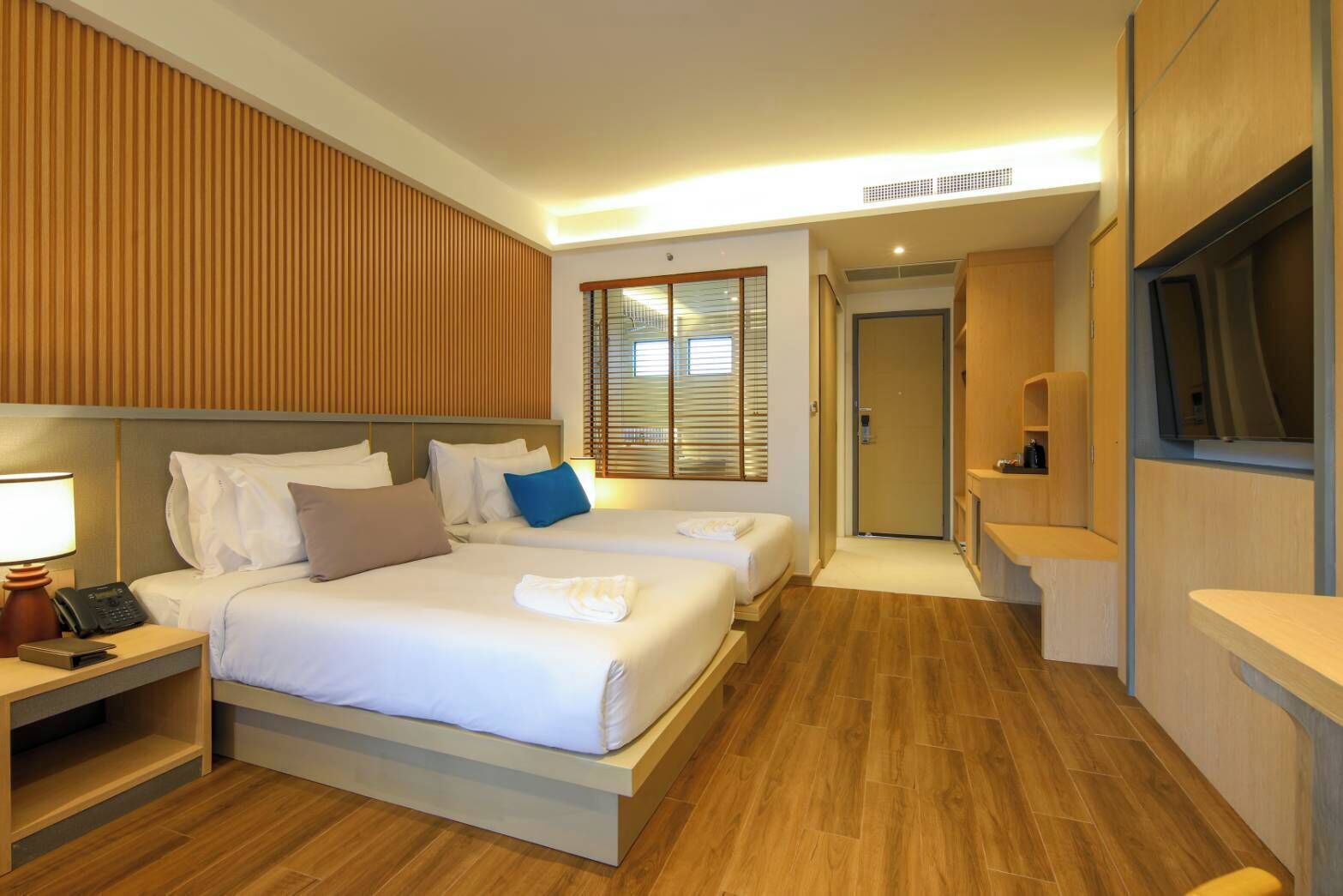 Une chambre d’hôtel avec deux lits, une table de chevet avec une lampe, une télévision et un mur recouvert de panneaux en bois.