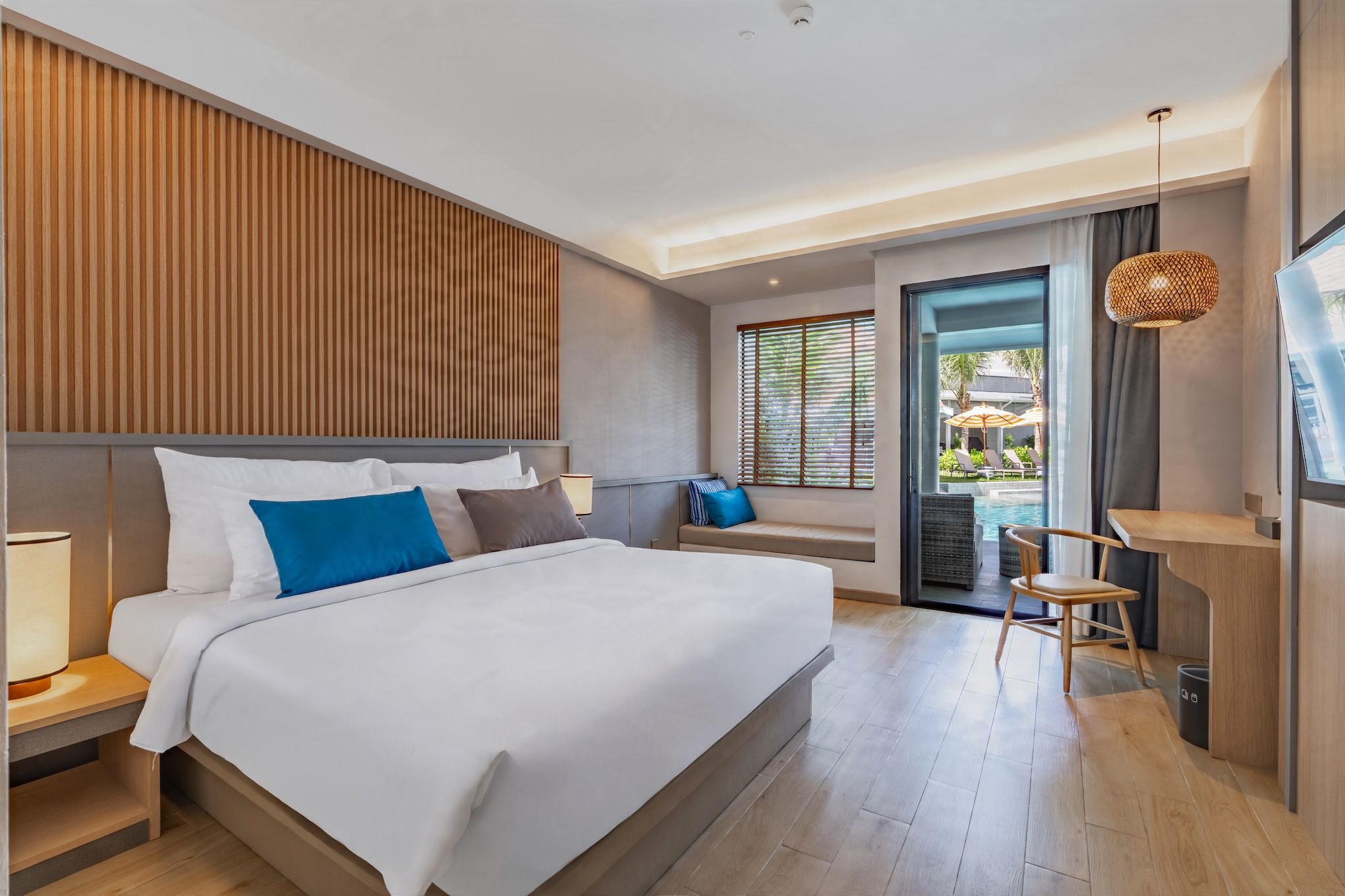 Habitación de hotel moderna con una cama grande, un escritorio y vistas al área de la piscina exterior.