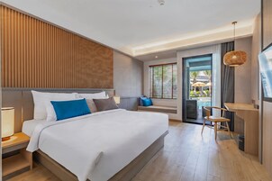 A modern hotel room with a large bed, a desk, and a view of the outdoor pool area.