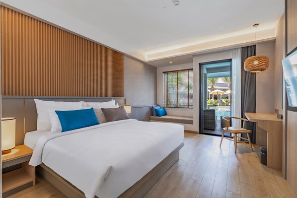 A modern hotel room with a large bed, a desk, and a view of an outdoor pool area. - Lalynn Resort & Villas, Phuket (Thep Krasattri)