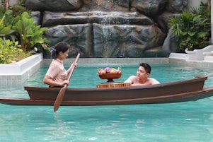 A boat with two people in a pool, a waterfall in the background, and a stone wall.