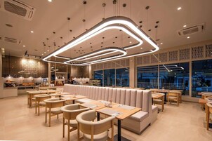 A modern restaurant interior with a central seating area, wooden tables, and a patterned wall.