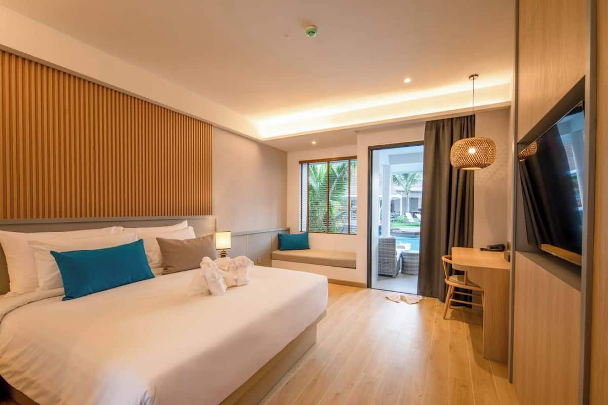Een moderne hotelkamer met een groot bed, een televisie, een zithoek met uitzicht op het zwembad en een balkon.