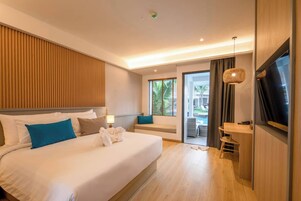 Una camera d'albergo moderna con un letto grande, una televisione, un angolo relax con vista sulla piscina e un balcone.