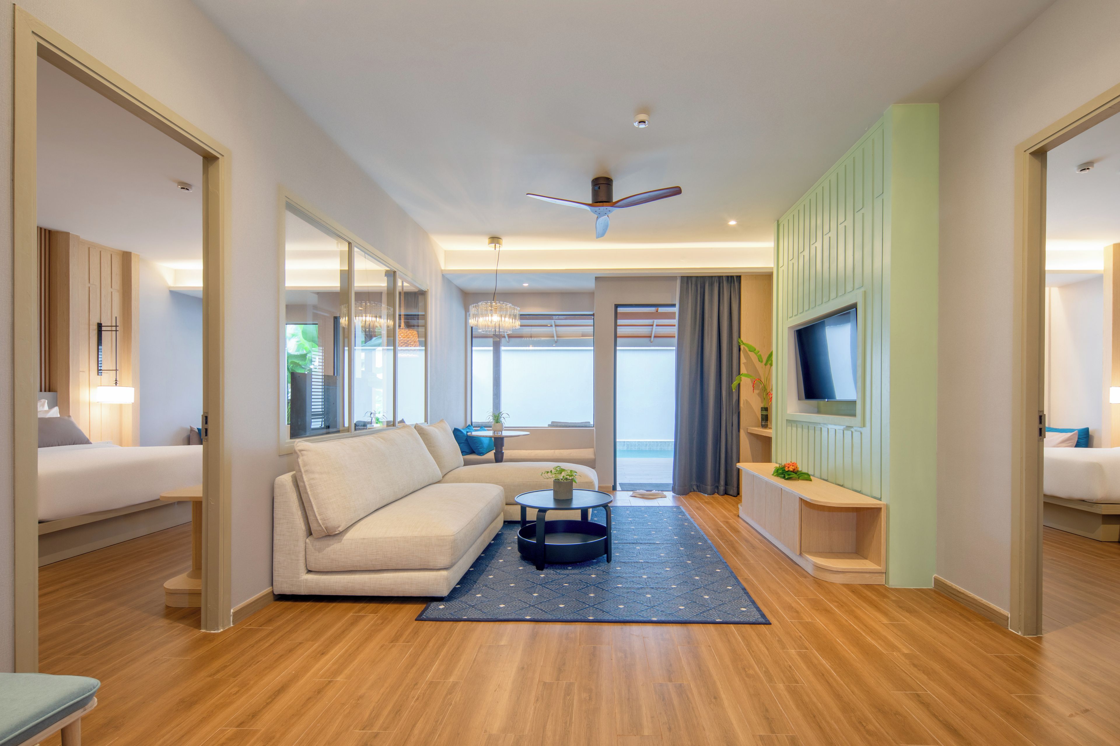 A modern hotel room with a sofa, a small table, a TV, and a balcony with a view.