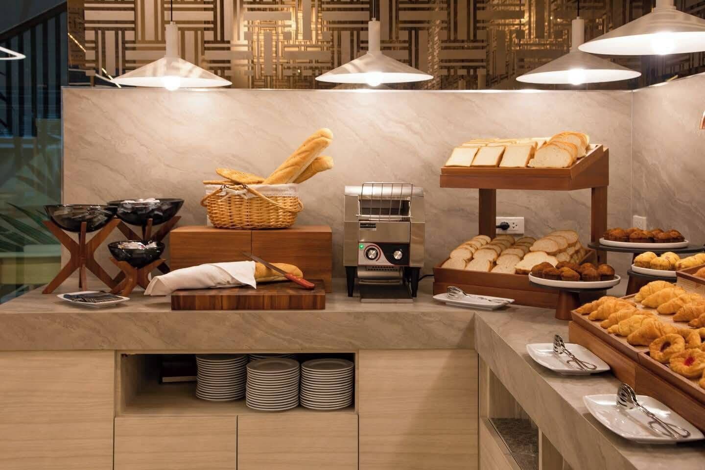 A buffet setup with bread, pastries, and a bread slicer.