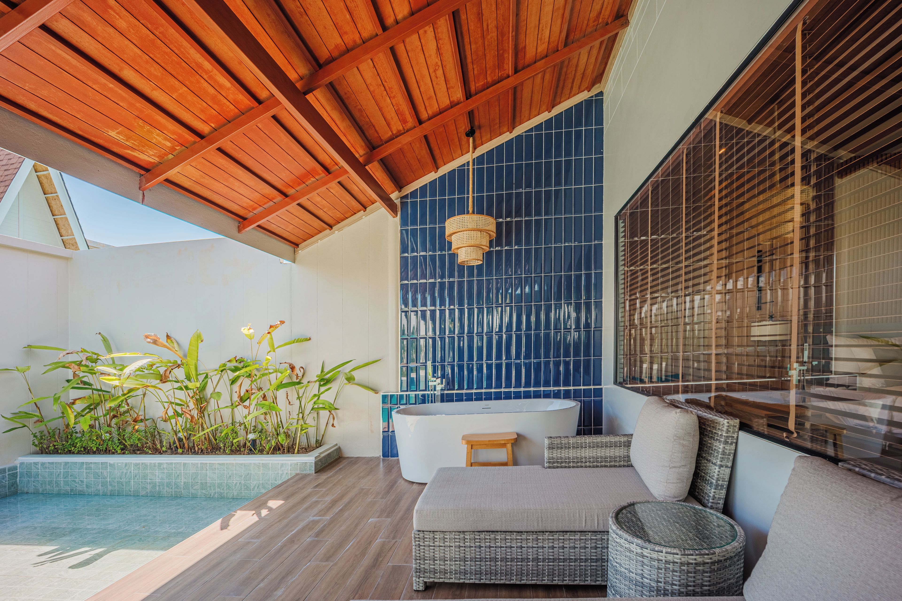 A modern outdoor area with a pool, a seating area with a sofa and chairs, and a large bathtub.