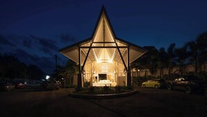 A modern building with a triangular roof structure, surrounded by a landscaped area with palm trees. - Lalynn Resort & Villas (Thep Krasattri)