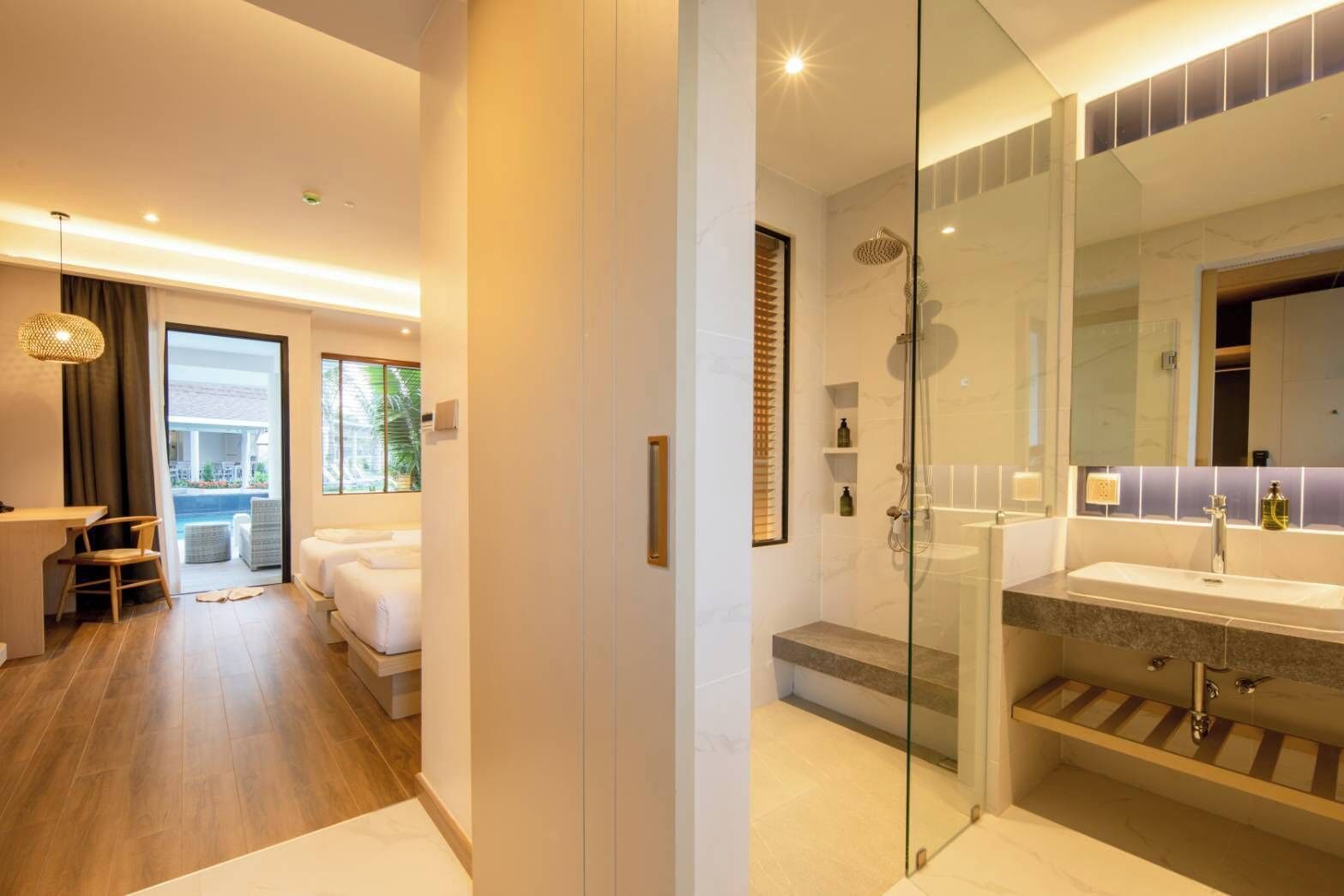 A modern hotel room with a glass shower enclosure, a large mirror, and a view of the outdoor pool area.