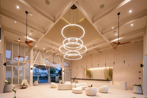 Un hall d’entrée spacieux avec un plafond haut, des luminaires modernes et un coin salon agrémenté de canapés blancs.